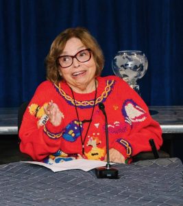 Judy Heumann speaking.  She is wearing a colorful red sweater.
